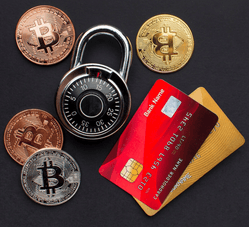 A combination padlock, several Bitcoin coins, and two credit cards are arranged on a dark surface, symbolizing digital security and financial protection.