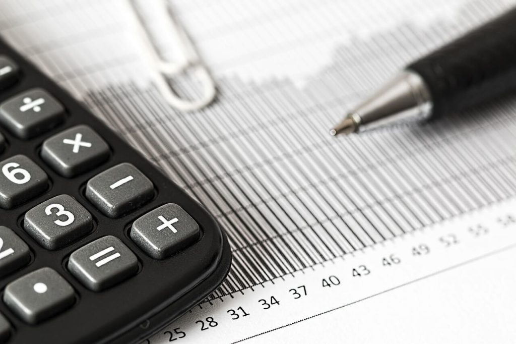 Close-up of a calculator, pen, and paperclip on a financial document with bar and line graphs, suggesting financial analysis or accounting work.