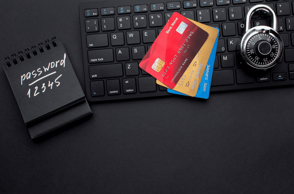 A notepad with "password 12345" written on it, two credit cards, a computer keyboard, and a padlock are arranged on a black surface, symbolizing security and online safety risks.