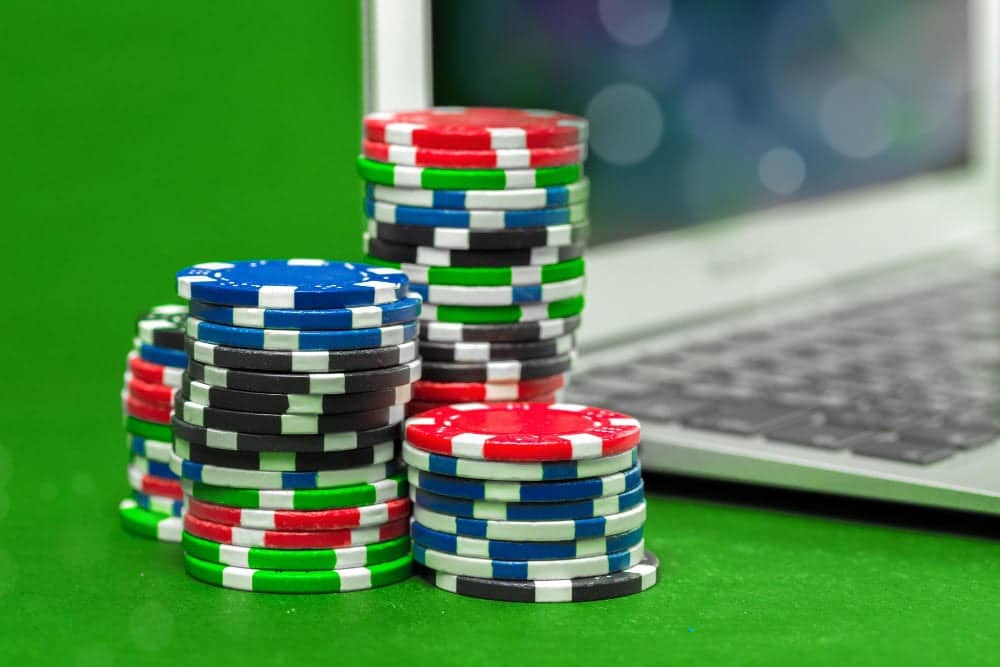 Stacks of multicolored poker chips are placed on a green surface next to a laptop keyboard, suggesting online gambling or virtual casino gaming.